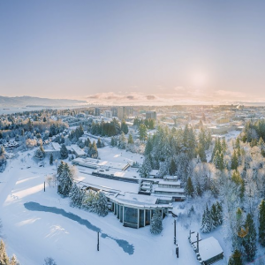 A drone photo of MOA with the UBC campus beyond, covered in fresh snow. The sun shines across a clear sky.