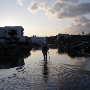 A person wades through shin-high water in tsunami-stricken Kesennuma City. It is dusk or dawn.