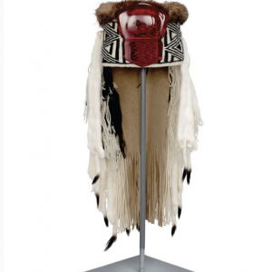 Chief's headdress is tall and round, open at crown and topped with a thick circle of brown fur. The exterior is covered in black and white weaving in 'lightning' design on the sides, and 'diamond within a diamond' design at front, covered by a thick copper-shaped frontlet made of dark red glass.